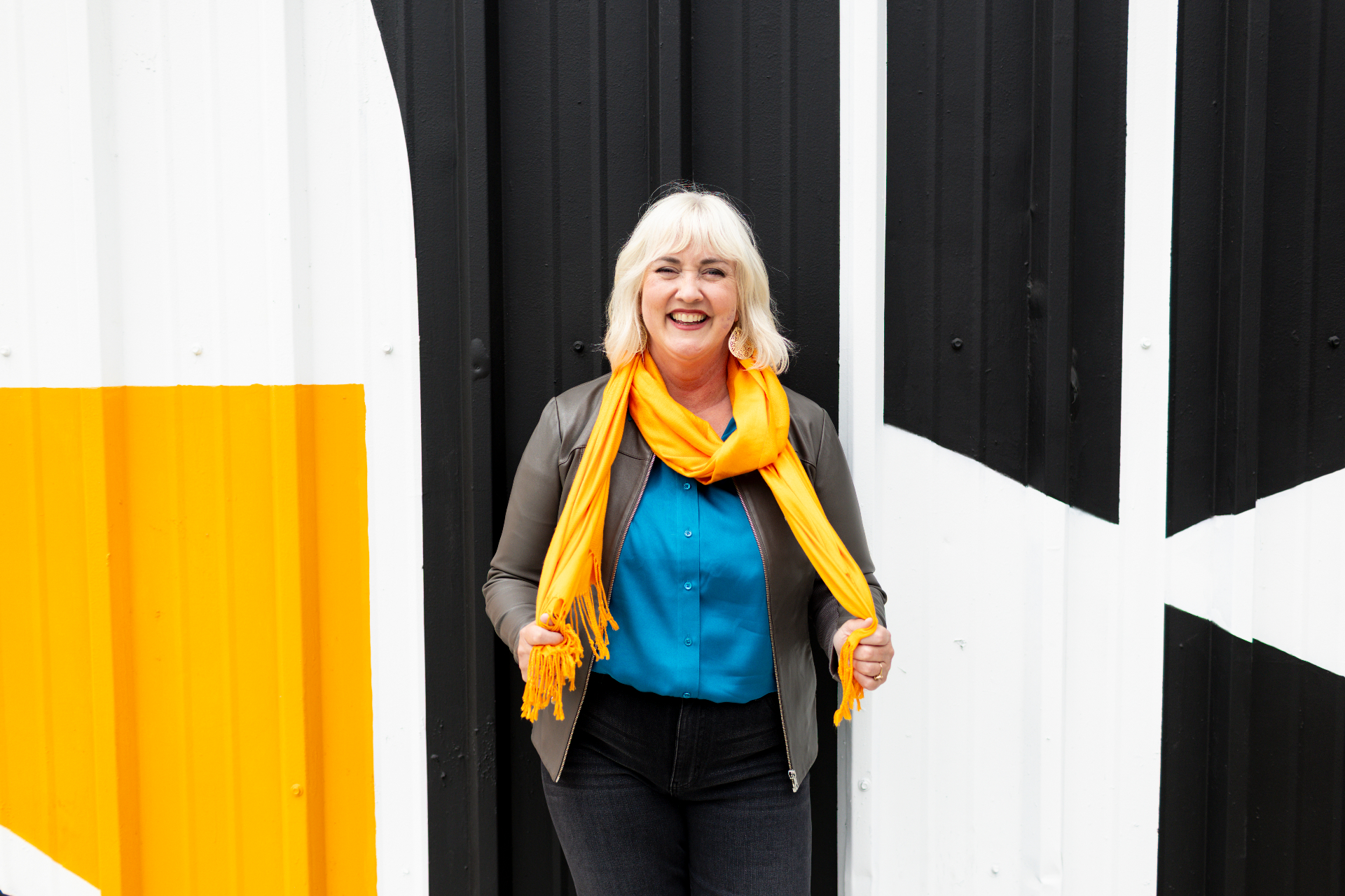 Quinn O'Briant Heller laughing in an orange scarf in front of a black and white mural